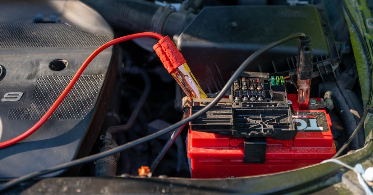 A lead-acid battery in an engine bay with clamped cables on both terminals