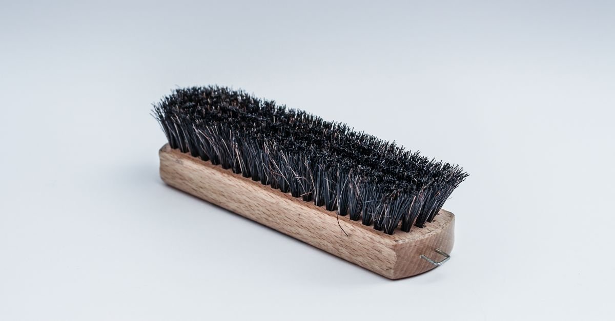Stiff-bristled wooden scrubbing brush resting on a pale surface