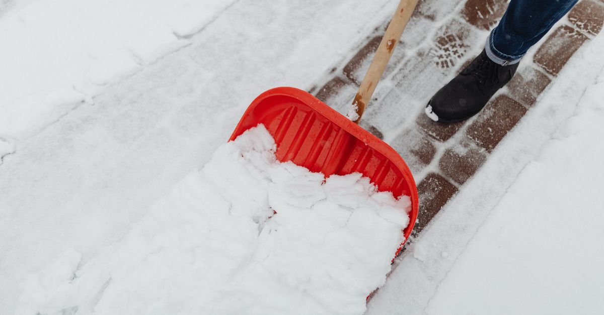 Person clearing snow from a residential driveway with a red shovel in winter
