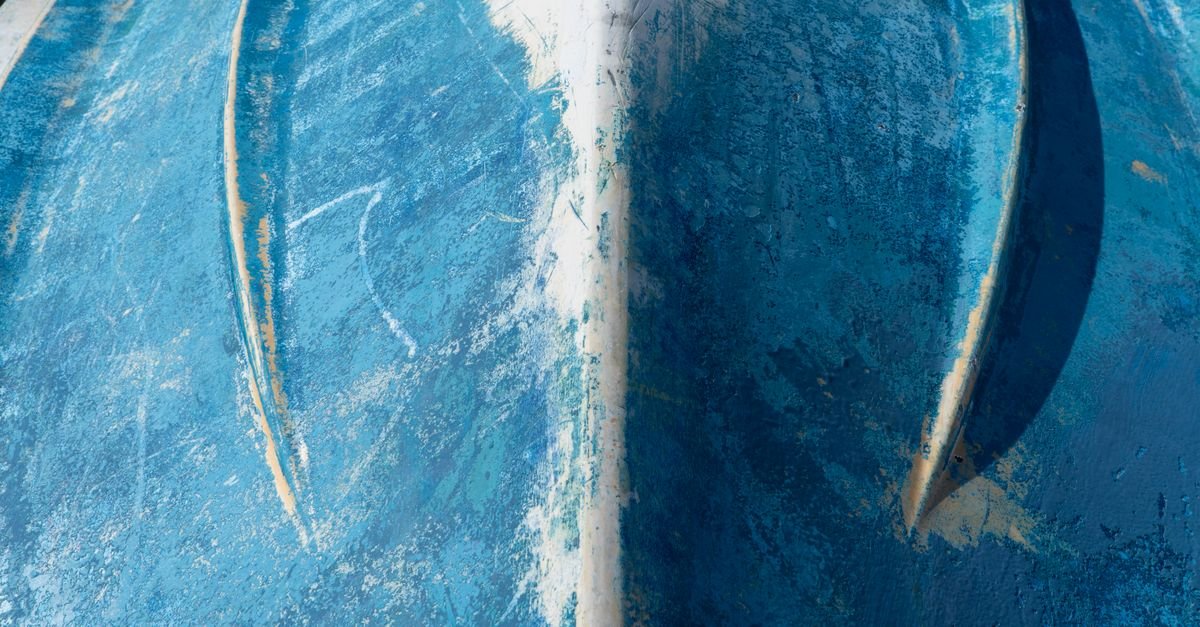 Close view of an aged blue boat hull underside showing worn, textured surface in raking sunlight