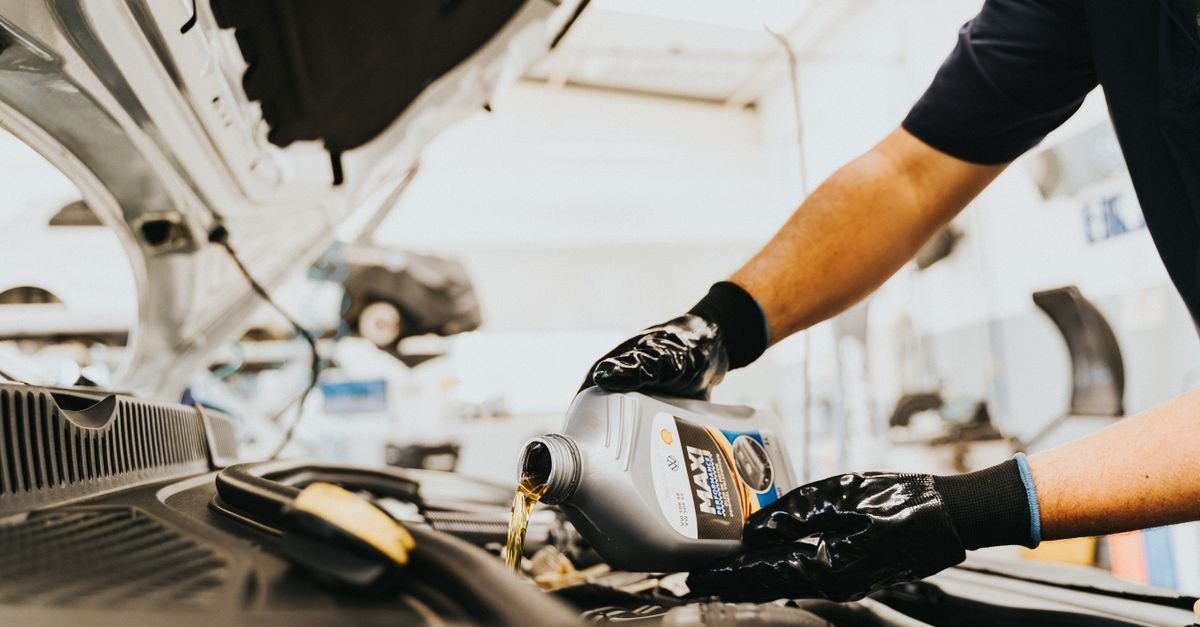 Gloved hands pouring fresh oil into a machine from a small bottle in a garage