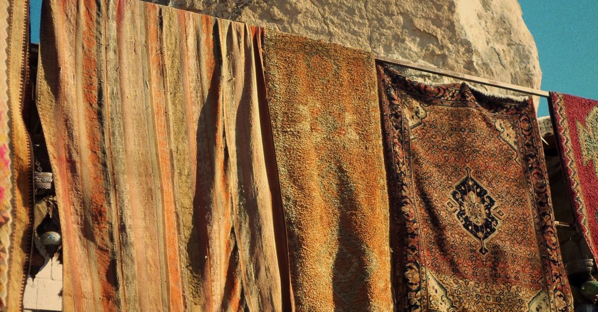 Colourful rugs hung out to dry in full sun against a rocky hillside
