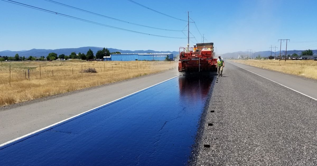 Asphalt maintenance crew applying a fresh seal coat to a paved surface