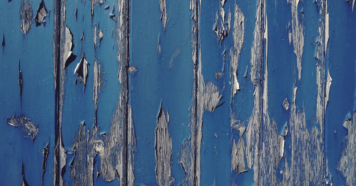 Blue paint peeling off a weathered wood surface in large flakes