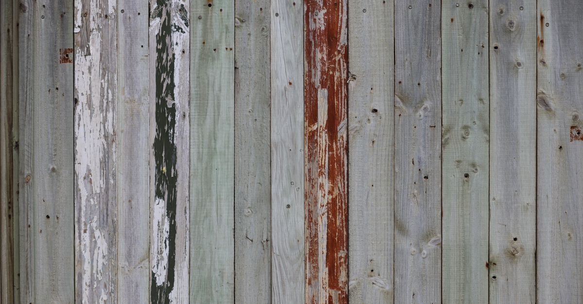 Weathered wood fence with peeling white and red paint traces