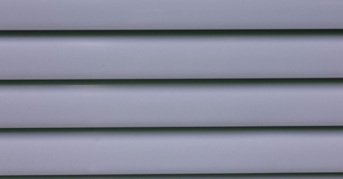 Close-up of overlapping gray vinyl siding panels showing the lap profile water can be forced behind