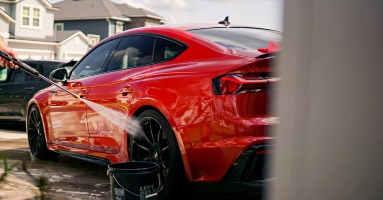 A vibrant red luxury car being washed outdoors in a suburban residential area