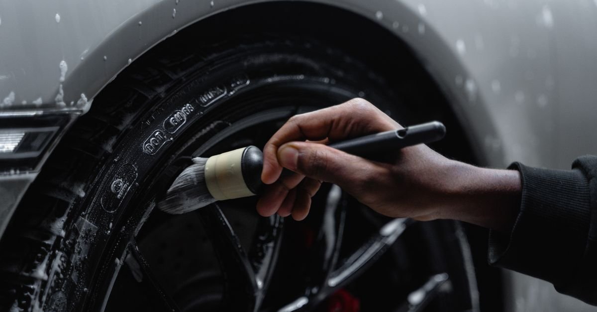 Detailed shot of a hand using a brush to clean a car tire and wheel during a wash