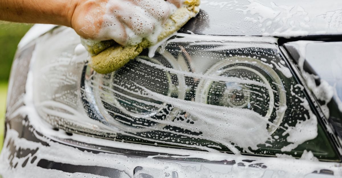 Hand scrubbing a soapy car headlight with a sponge during a wash
