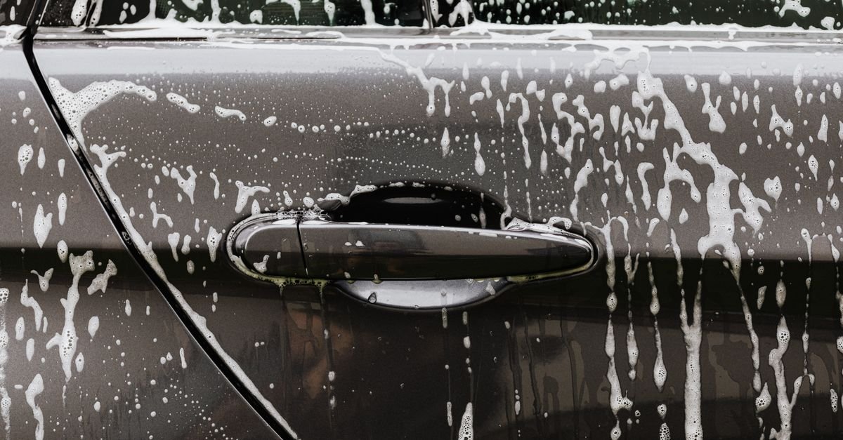 Close-up of thick soap suds running down a glossy black car door