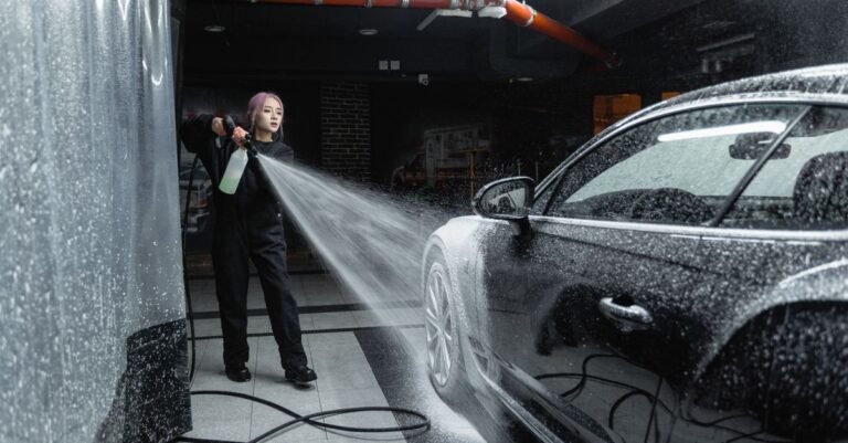 Woman using a pressure washer to rinse soap from a black car in a wash bay