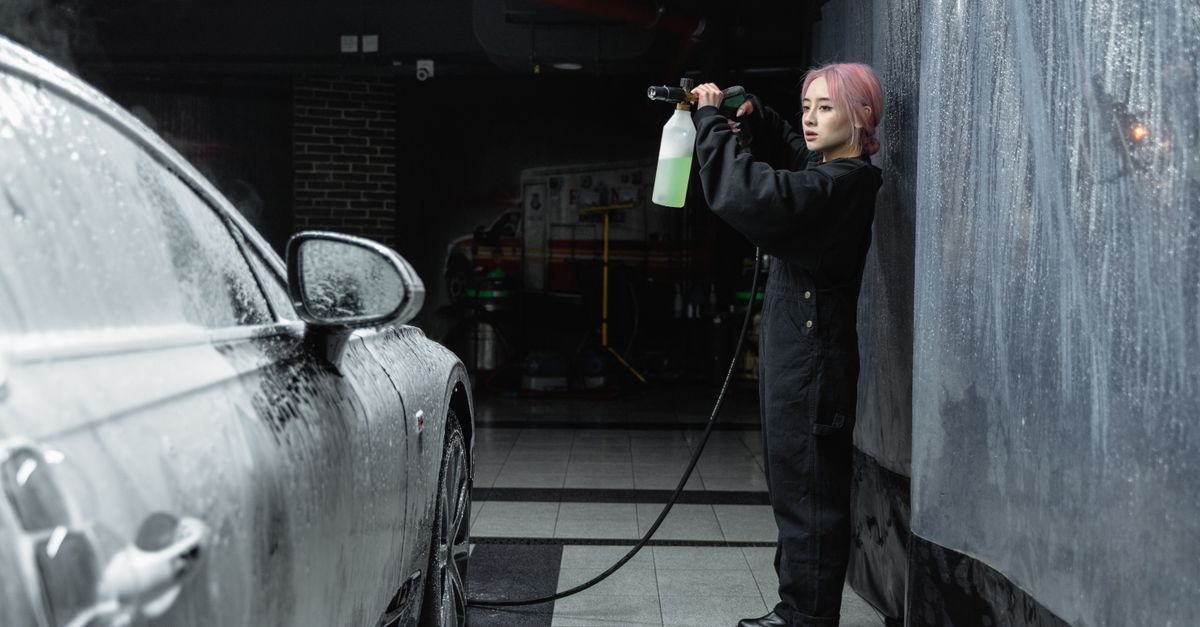 Person applying thick white snow foam to a car with a pressure washer lance