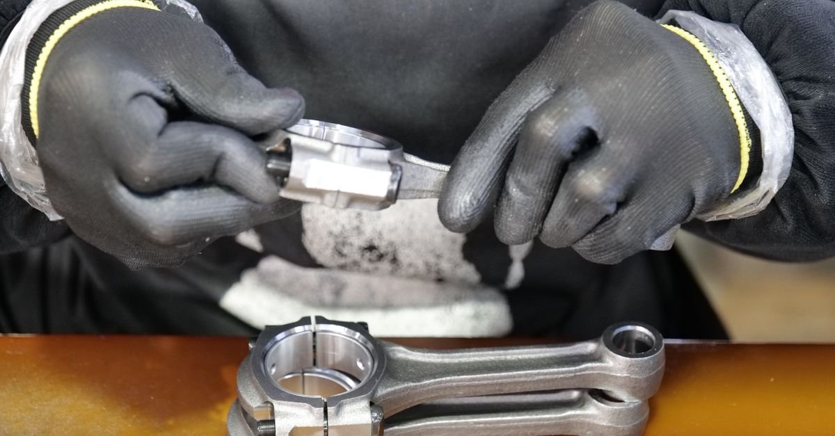 Close-up of a technician's hands assembling a metal connecting rod with precision and care