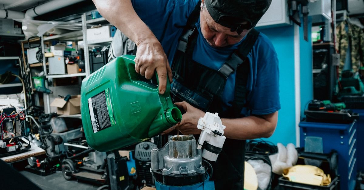 Mechanic in blue uniform pouring oil into an engine component during routine workshop maintenance