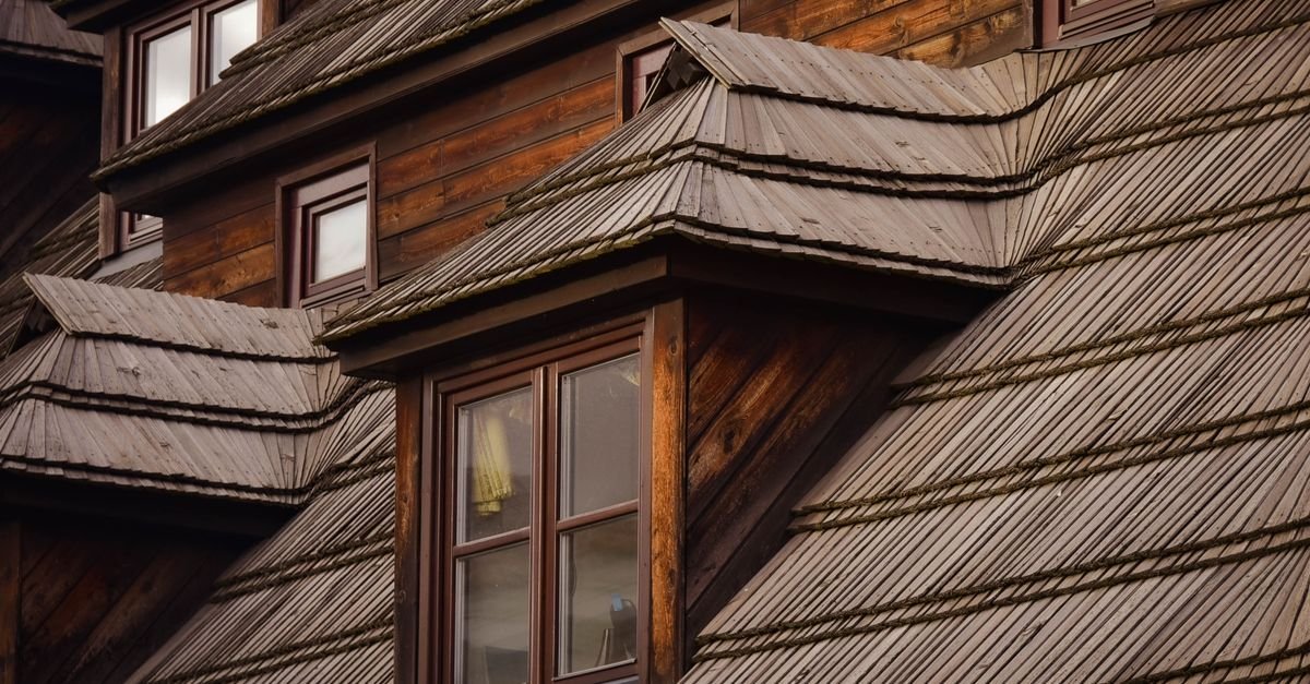 Rustic wooden house with weathered shingle roof courses meeting the wall below