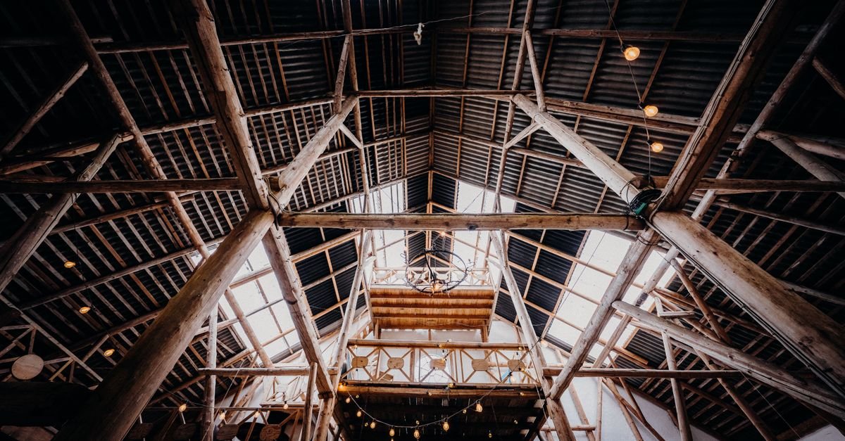 Interior of a barn showing bare timber beams meeting a steel structural frame overhead