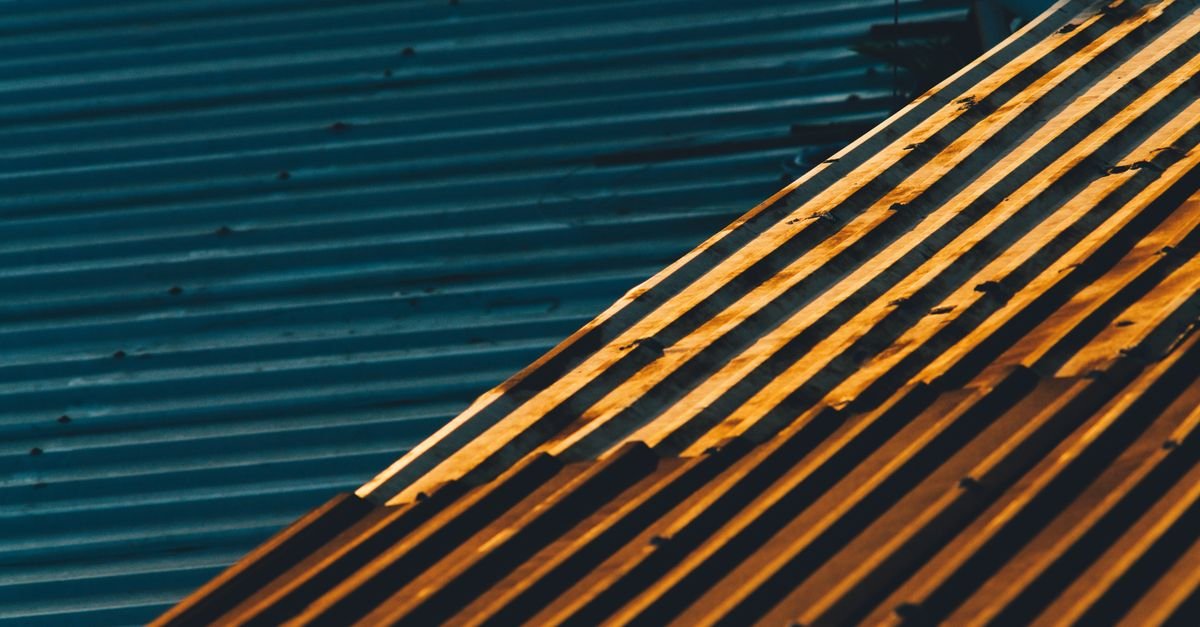 Overlapping corrugated metal sheets in raking sunlight, showing the side laps water can be forced under