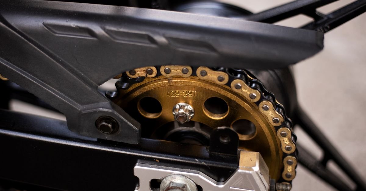 Close-up of a gold motorcycle drive chain meshing with its rear sprocket, side plates and rollers in sharp focus