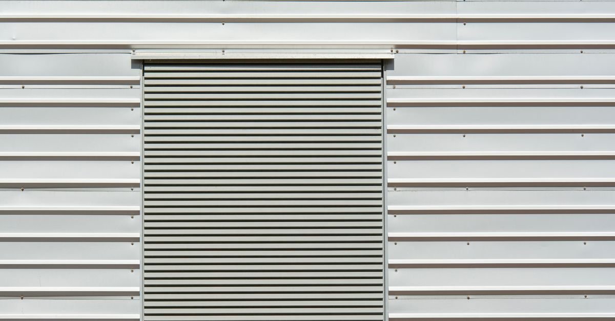 Close-up of a thin white sheet metal wall panel next to a roller shutter door