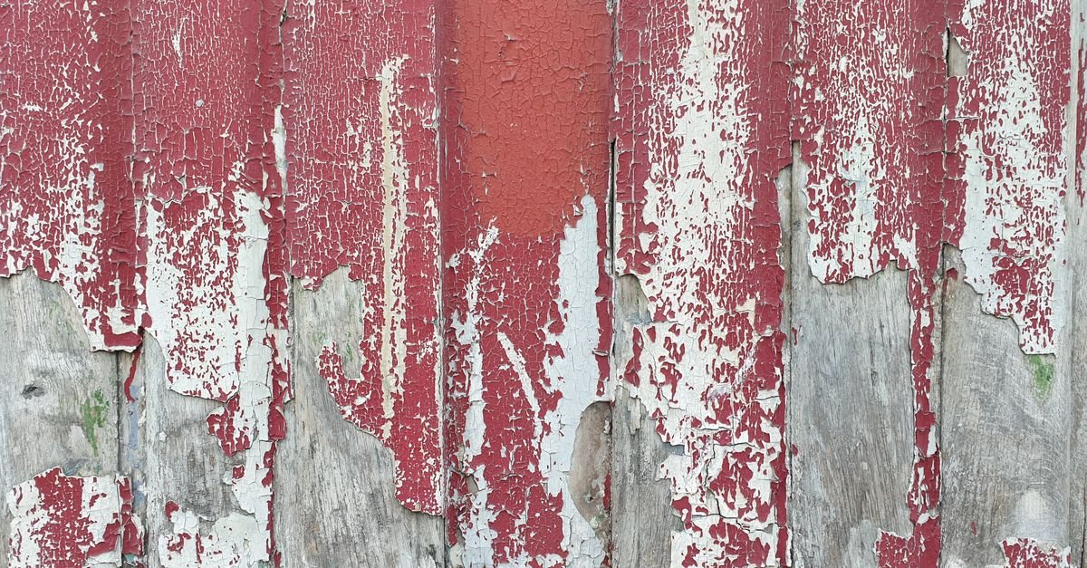 Weathered deck boards with a peeling red film finish lifting away from the bare wood underneath
