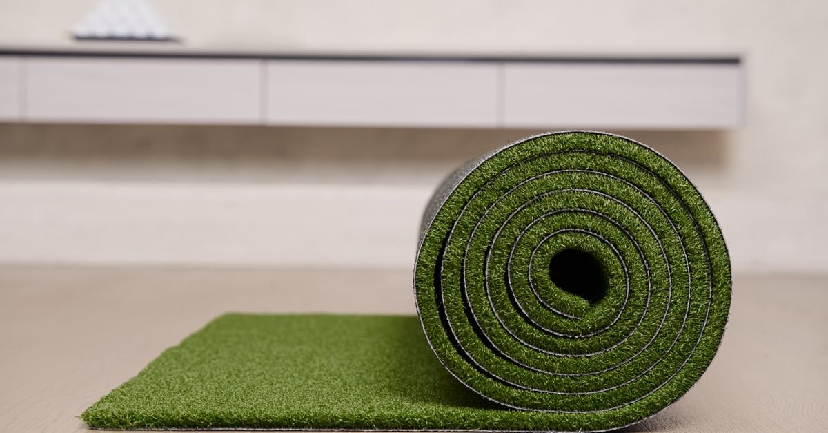 Roll of artificial turf partly unrolled on a floor, showing the fibres and the coated backing