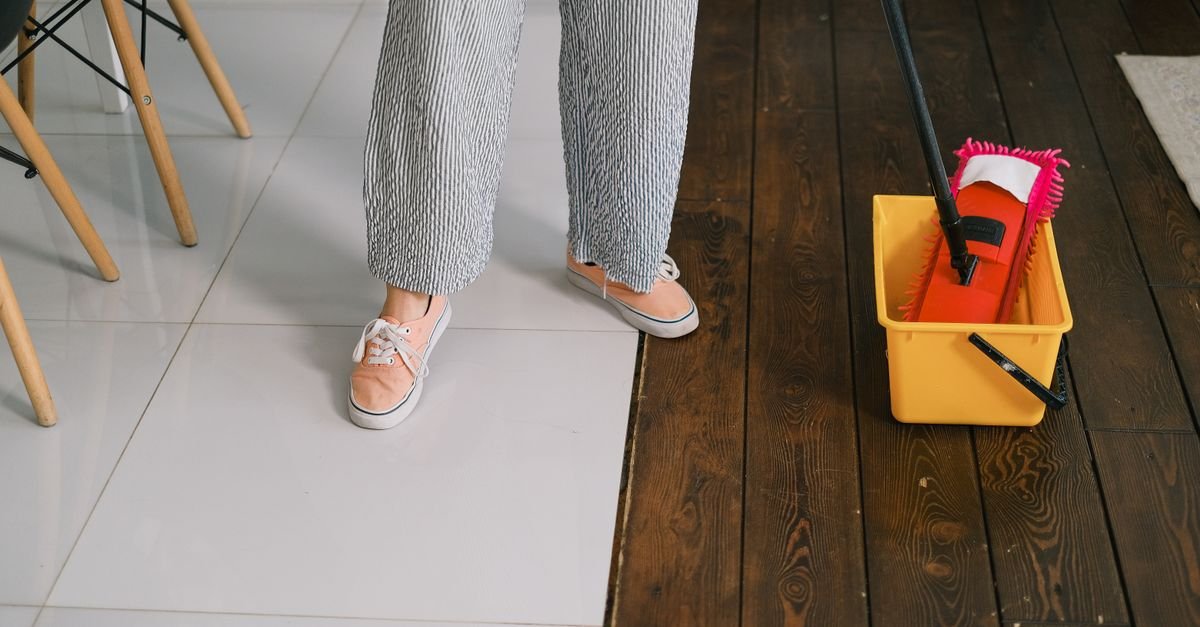 Mop being dipped into a bucket of cleaning solution beside a hard floor