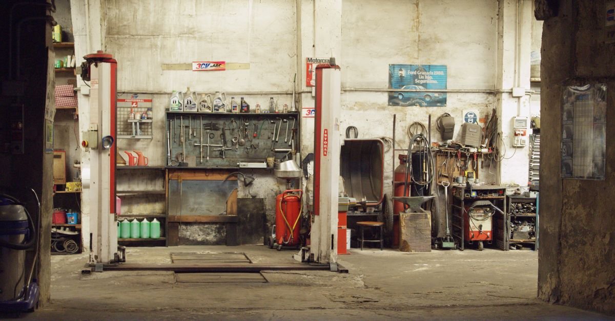 A rustic car workshop with a lift, tools and a concrete floor that has absorbed years of drips