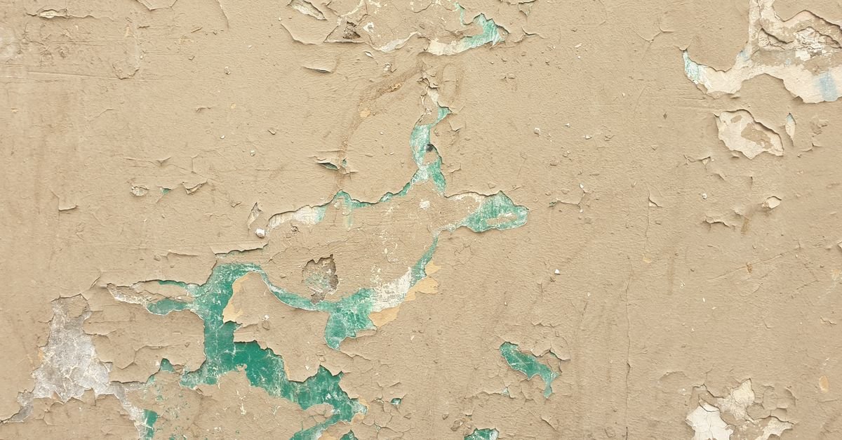 Paint lifting and flaking away from a weathered masonry wall