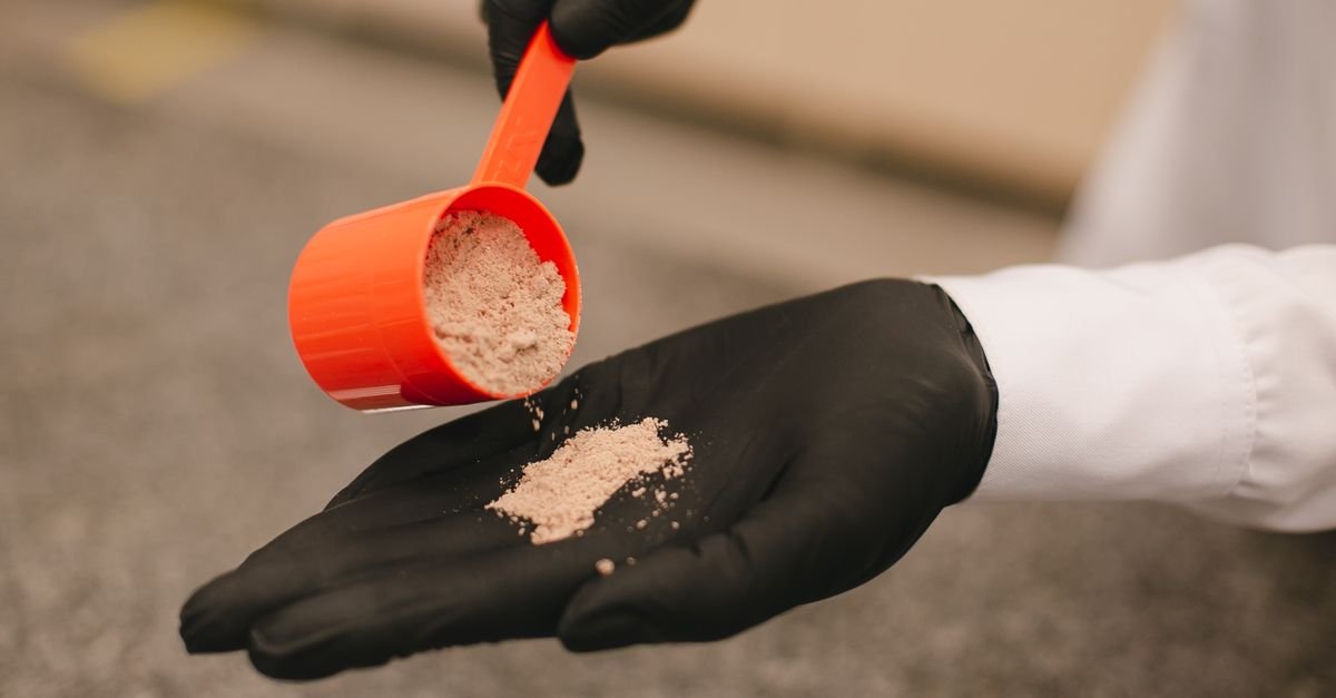 A gloved hand pouring cleaning powder from a red scoop