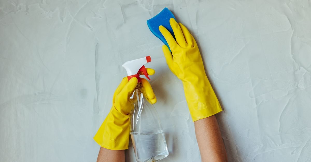 Gloved hands applying cleaning solution to a masonry surface with a spray bottle and sponge