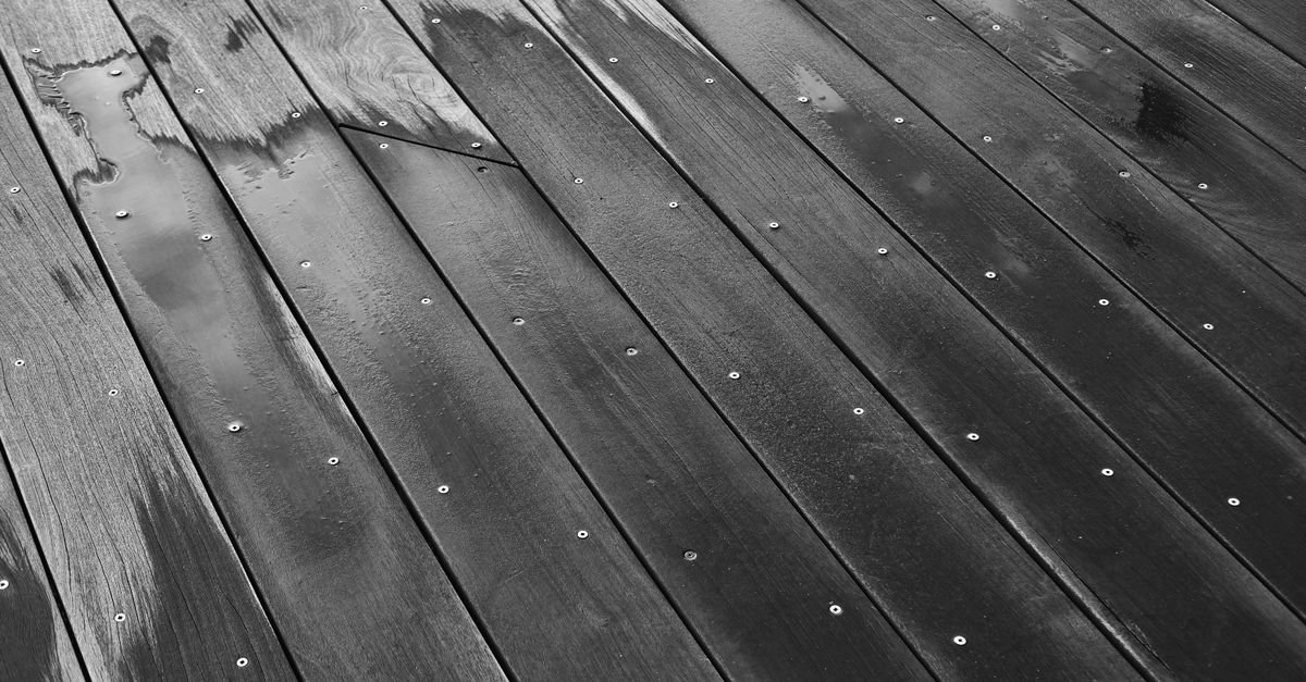 Wet timber deck boards with visible grain and fixings after a rinse, the state to assess a test patch from