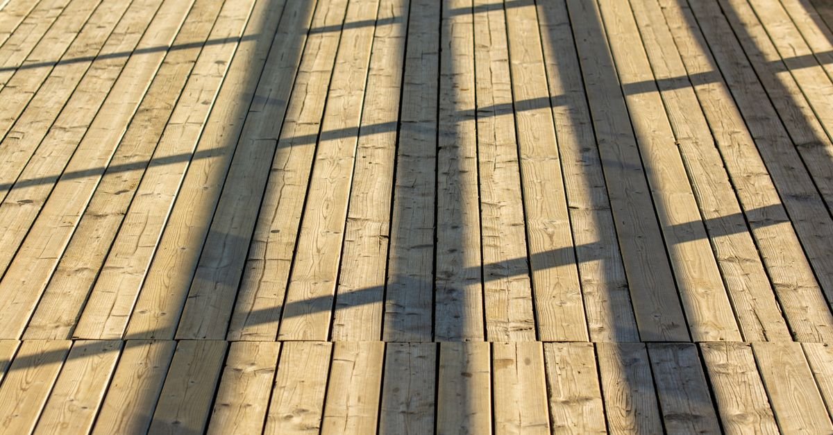Sunlit timber deck boards running lengthwise away from the viewer, the direction every pass should follow