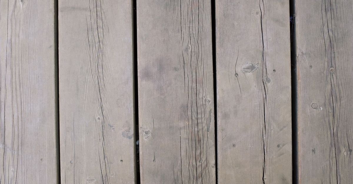 Weathered softwood deck planks photographed close up, showing open grain and silvered surface fibre