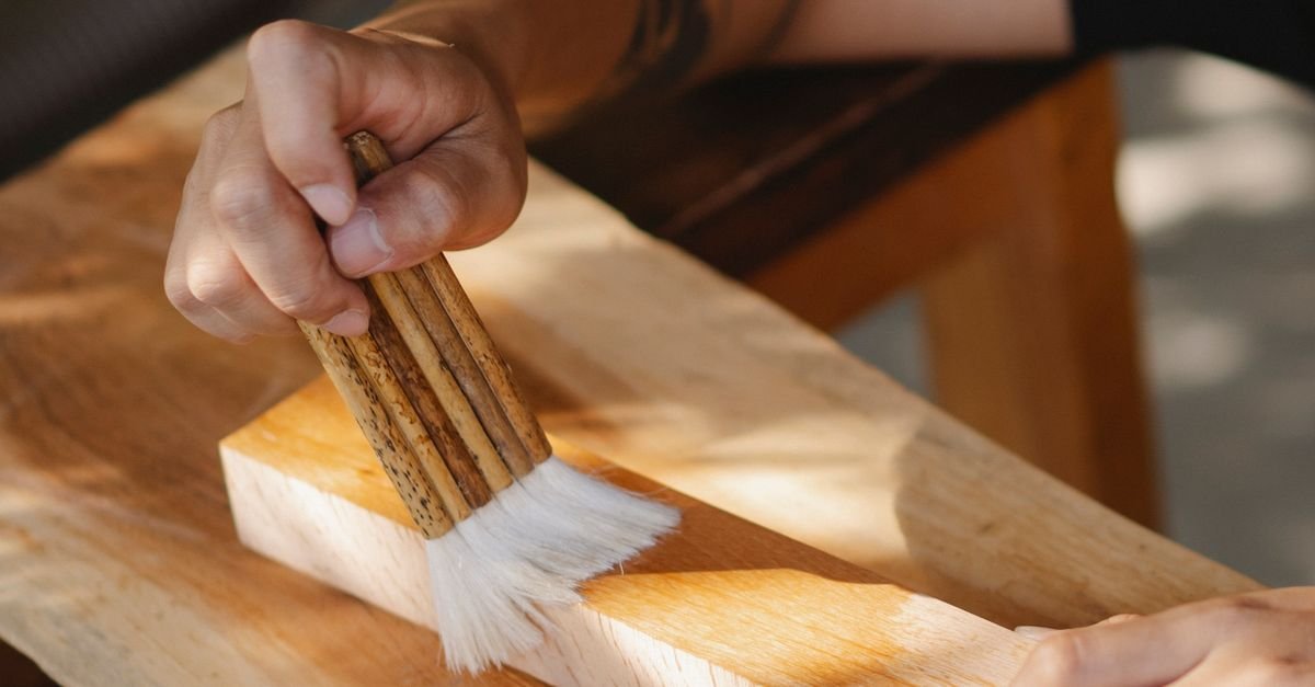 Person brushing a protective finish onto bare timber, the coat that has to bond to a cleaned surface