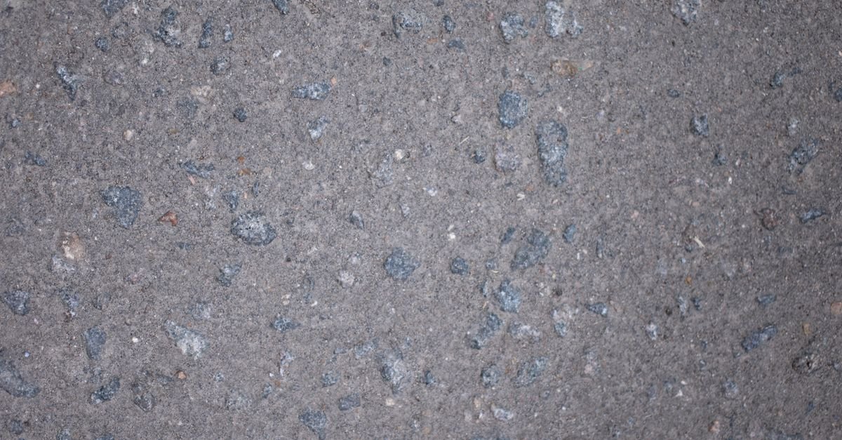 Close-up of a rough grey paved surface with loose grit and stone scattered across it