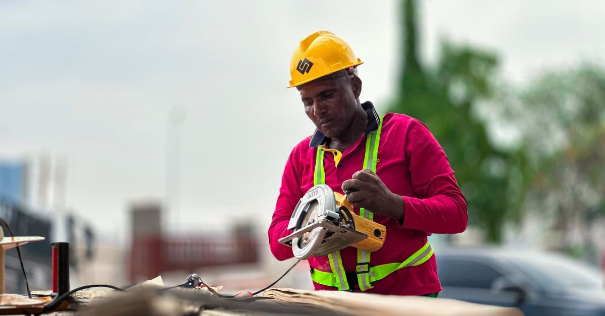 A construction worker in a hard hat operating a circular saw on a building site