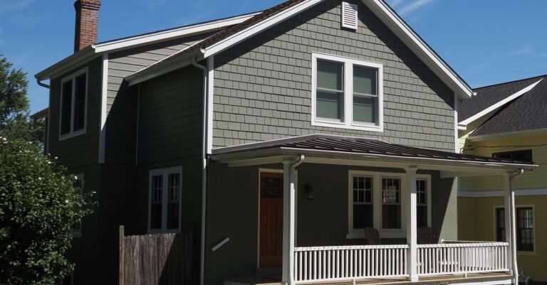 A quaint suburban home with a front porch and pale lap siding under a clear sky