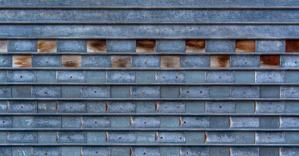 Close-up of a weathered metal garage door showing horizontal panel ribs, rivet heads and rust bleeding from each joint line