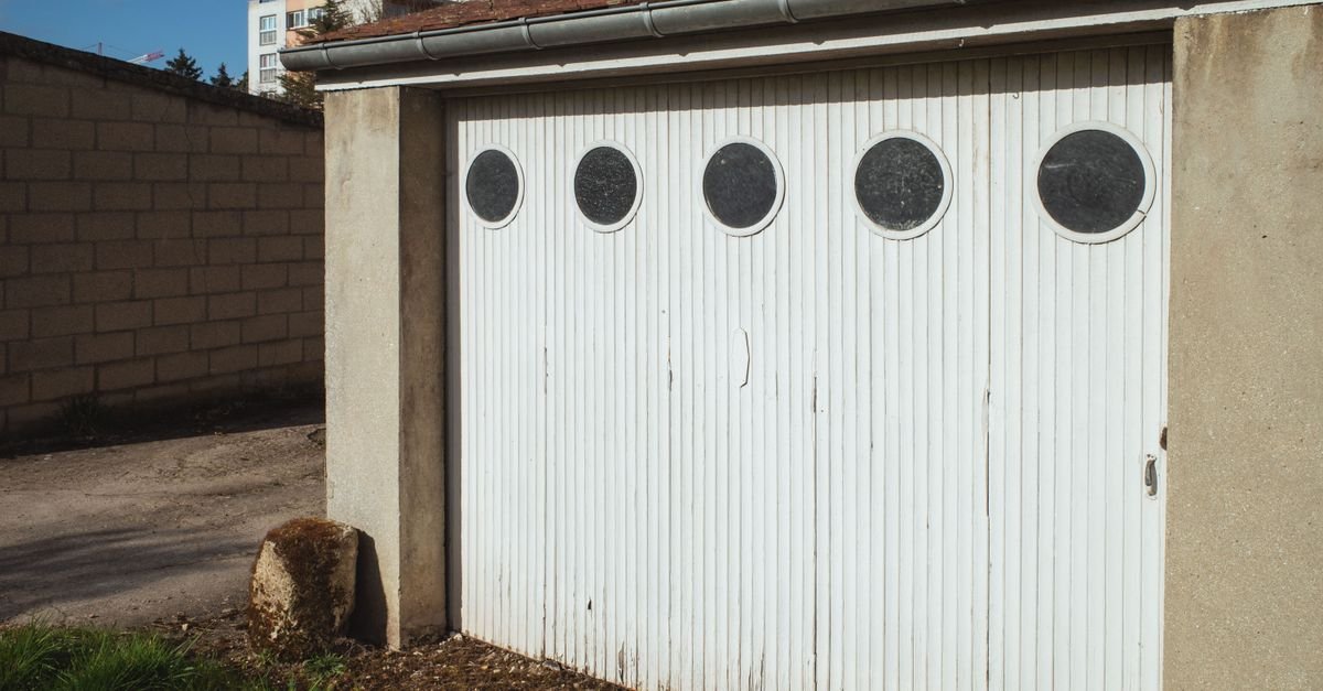 A weathered white ribbed garage door with five round porthole windows, weathered paint along the vertical panel joints