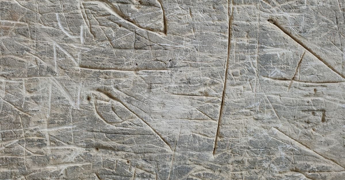 Flat pale stone surface covered in fine crossing scratches and incised marks