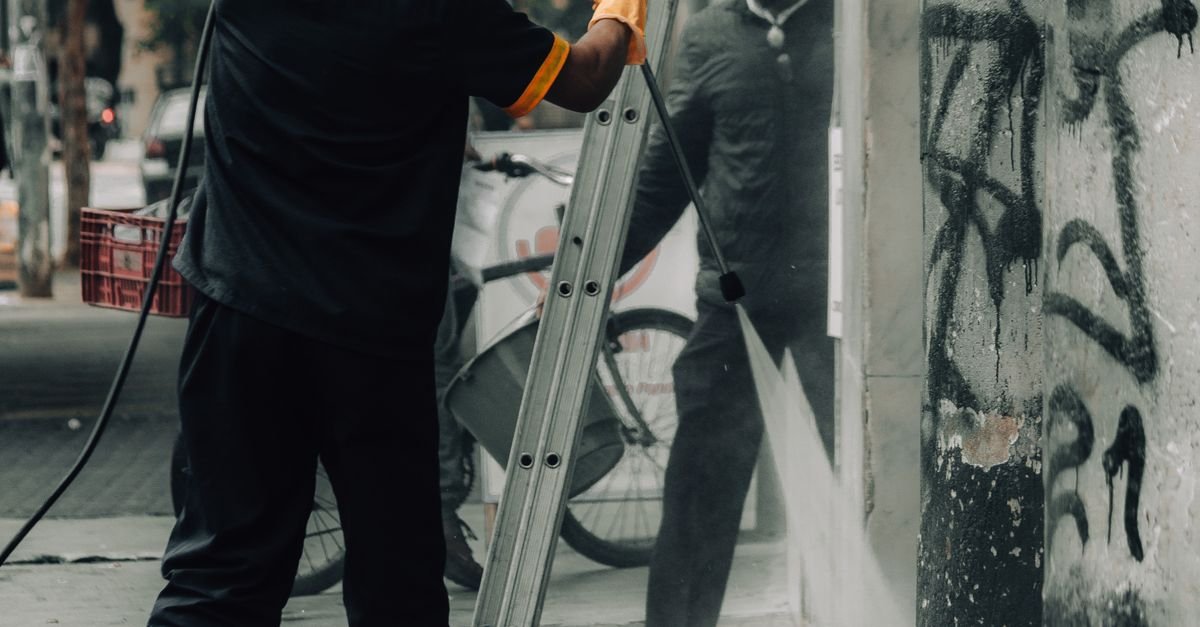 Workers using a high-pressure hose to strip staining from the face of a building wall