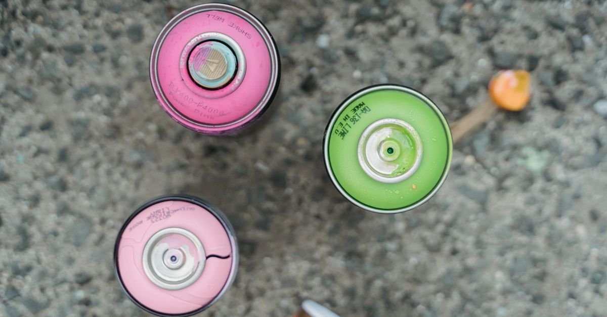 Spray paint cans arranged on a bare concrete surface, the kind of overspray problem that starts most paint removal jobs
