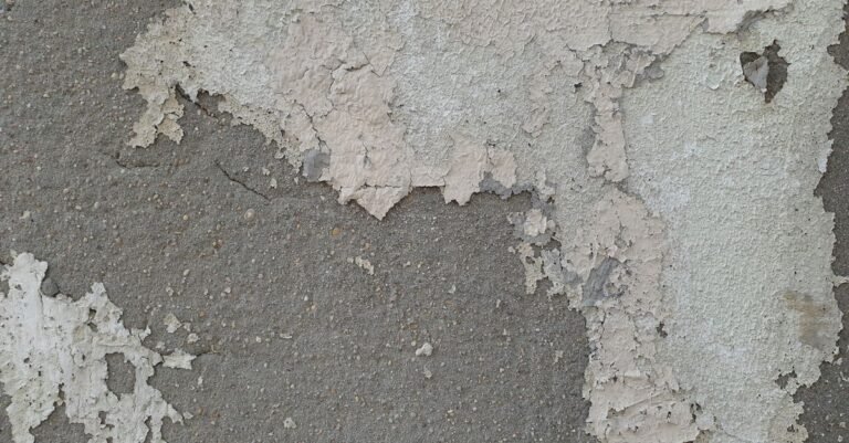 Worn concrete wall with old paint peeling back to reveal the bare grey surface underneath