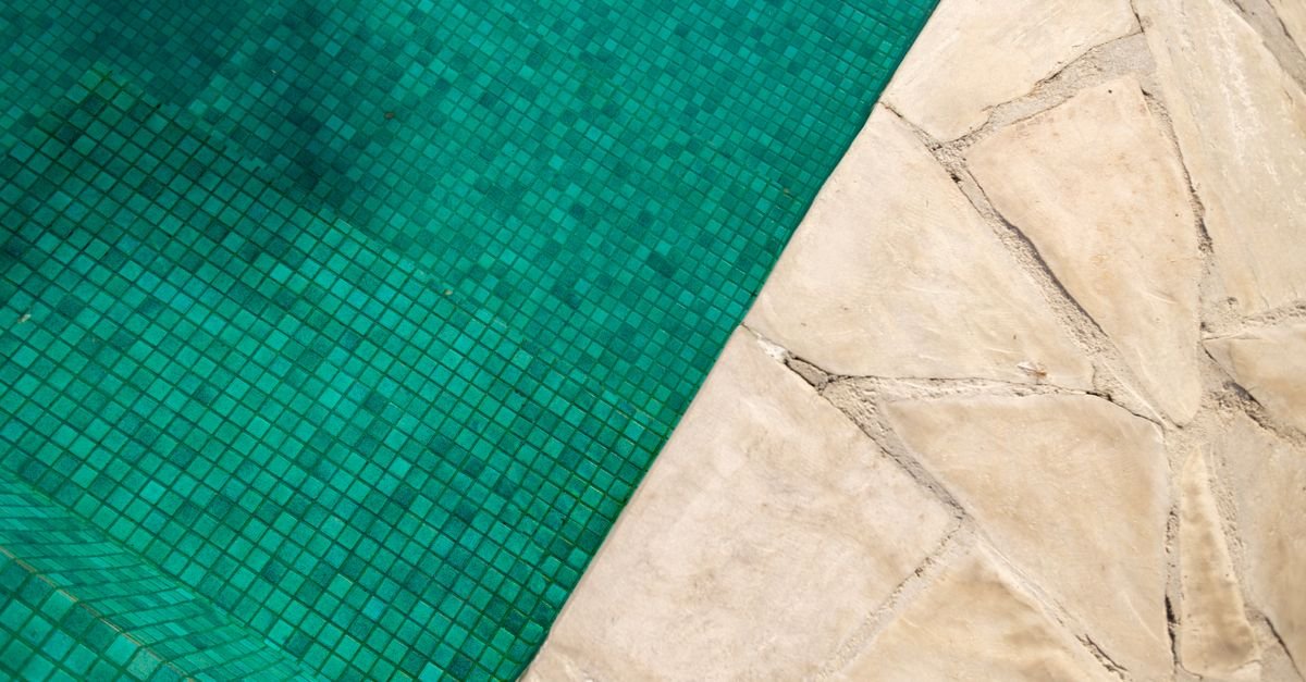 Overhead view of a turquoise swimming pool edged with pale stone paving in bright sun