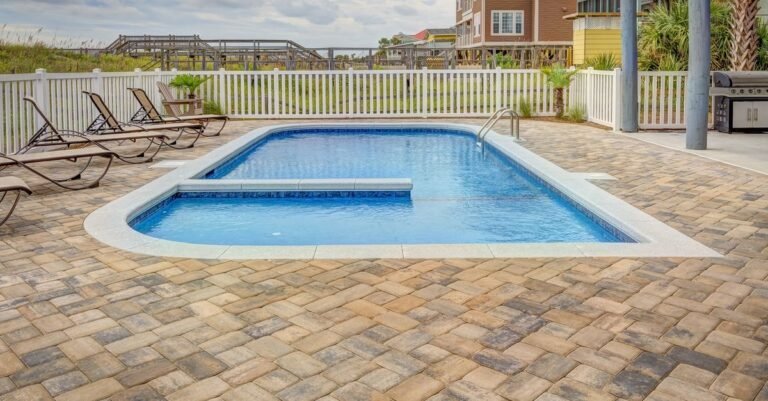 Poolside patio of pale paving with sun loungers set out along the water's edge