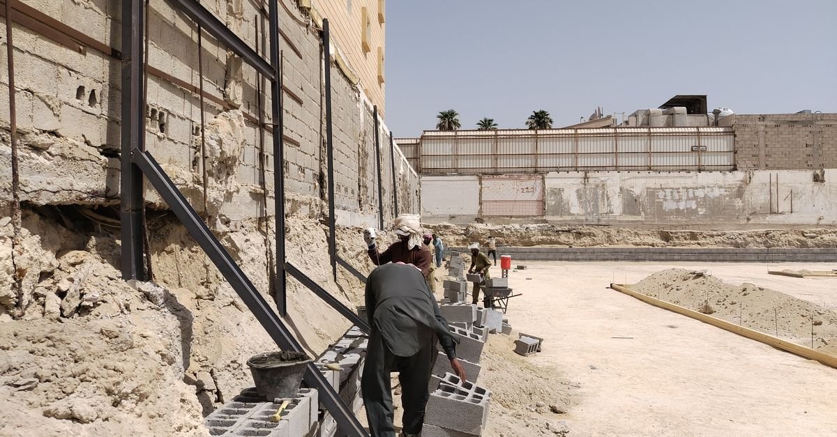 Workers setting courses of concrete block for a retaining wall with the gravel backfill zone open behind them
