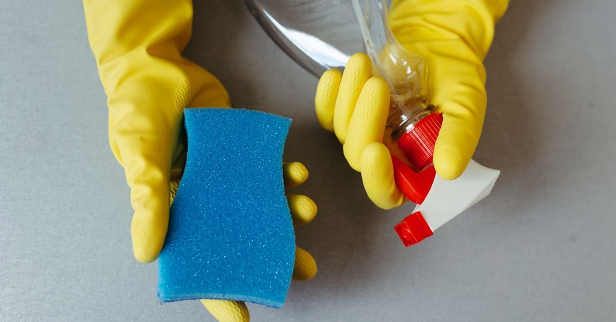 Gloved hands holding a spray bottle and sponge, ready for applying a cleaning solution
