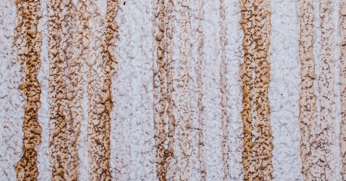 Vertical orange-brown rust staining running down a textured concrete wall