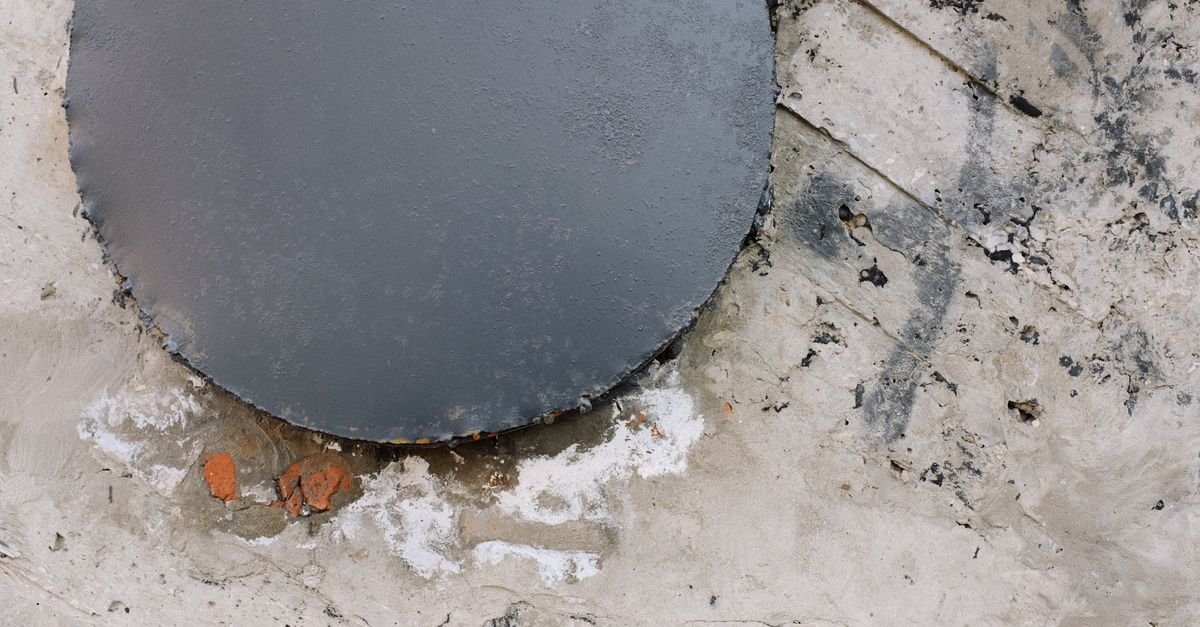 A rusted metal cover set into a textured concrete surface, staining the slab around it