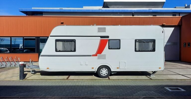 A white caravan with red graphics parked beside an industrial building under a clear sky